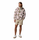 A man wears the Columbia Mens Helvetia II Printed Half Snap Fleece with a pink and green floral pattern, beige shorts, and white sneakers, standing against a plain white background.