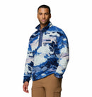 A man wears the Columbia Mens Helvetia II Printed Half Snap Fleece in blue, white, and purple with brown pants, facing forward with a neutral expression against a plain white background.