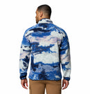 A man faces away, wearing the Columbia Mens Helvetia II Printed Half Snap Fleece in a blue, white, and purple cloud pattern with tan cargo pants. The background is plain white.