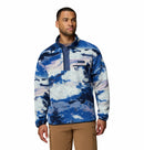 A man wears the Columbia Mens Helvetia II Printed Half Snap Fleece in blue, white, and purple with a buttoned collar and brown pants, standing against a plain white background.