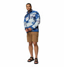 A man stands against a white background wearing Columbia’s Mens Helvetia II Printed Half Snap Fleece, tan cargo shorts, and black sandals. He has short hair and poses with hands together, looking toward the camera.