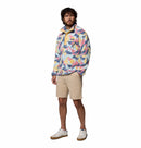 A man with curly hair and a beard wears the Columbia Mens Helvetia II Printed Half Snap Fleece pullover, tan shorts, and white sneakers. He stands facing slightly to the side against a plain white background.