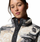 A woman wears the Columbia Womens Helvetia II Cropped Sherpa Half Snap Printed Fleece in white, grey, and black with a high collar and snap buttons, looking at the camera with a neutral expression.