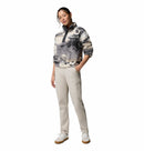 A woman stands with one hand in her pocket, wearing the Columbia Womens Helvetia II Cropped Sherpa Half Snap Printed Fleece, light beige pants, and white sneakers against a plain white background.