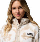 A woman with long blonde hair wears the Columbia Womens Helvetia II Cropped Sherpa Half Snap Printed Fleece, beige and white with a zippered chest pocket, standing against a white background.