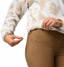 A person adjusts the drawstring at the hem of a Columbia Womens Helvetia II Cropped Sherpa Half Snap Printed Fleece in beige and white, paired with brown pants; only their torso and hands are visible.