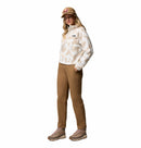A woman wears the Columbia Womens Helvetia II Cropped Sherpa Half Snap Printed Fleece with a tan baseball cap, brown pants, and tan hiking boots, standing with one hand in her pocket against a white background.