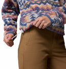 A person is adjusting the hem drawstring of a Columbia Womens Helvetia II Cropped Sherpa Half Snap Printed Fleece jacket; only their torso and hands are visible, paired with brown pants.