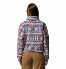 A person with long brown hair, seen from behind, wears Columbias Womens Helvetia II Cropped Sherpa Half Snap Printed Fleece, featuring colorful patterns on white, paired with brown pants.