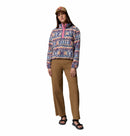 A woman in a Columbia Womens Helvetia II Cropped Sherpa Half Snap Printed Fleece, brown pants, black sandals, and a tan baseball cap stands against a white background.