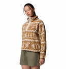 A woman wearing the Columbia Womens Helvetia II Cropped Sherpa Half Snap Printed Fleece in tan and white with a high collar and khaki shorts, standing against a white background.