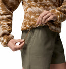 A person adjusts the drawstring of the Womens Helvetia II Cropped Sherpa Half Snap Printed Fleece by Columbia, wearing olive green shorts. The PFAS-free fleece and their hands are shown against a white background.