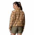 A woman with a ponytail faces away, wearing Columbias Womens Helvetia II Cropped Sherpa Half Snap Printed Fleece in brown and white with olive green shorts, standing against a plain white background.