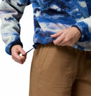 A person, visible from the torso and hands, tightens the drawstring at the hem of a Columbia Womens Helvetia II Cropped Sherpa Half Snap Printed Fleece while wearing tan pants.