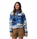 A woman wears the Columbia Womens Helvetia II Cropped Sherpa Half Snap Printed Fleece, featuring a blue, white, and purple print with a buttoned collar, paired with tan shorts against a plain white background.