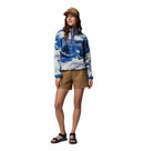 A woman smiles against a white background, wearing a tan baseball cap, brown shorts, black sandals, and the Columbia Womens Helvetia II Cropped Sherpa Half Snap Printed Fleece in blue and white.