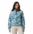 A woman models the Columbia Womens Helvetia II Cropped Sherpa Half Snap Printed Fleece in light blue with a high collar and snap buttons, paired with light-colored pants, against a white background.