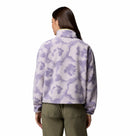 A woman is seen from behind wearing the Columbia Womens Helvetia II Cropped Sherpa Half Snap Printed Fleece in light purple and white, paired with olive green pants, standing against a plain white background.