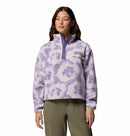 A woman wears the Columbia Womens Helvetia II Cropped Sherpa Half Snap Printed Fleece in light purple and white with a green zipper, paired with olive green pants, against a white background.