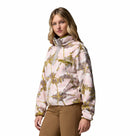 A woman wears the Columbia Womens Helvetia II Cropped Sherpa Half Snap Printed Fleece in light pink and yellow, featuring a high collar, paired with brown pants, standing slightly to the side against a plain white background.