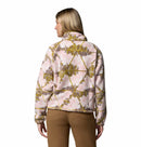 A woman faces away, wearing the Columbia Womens Helvetia II Cropped Sherpa Half Snap Printed Fleece in pink and yellow patterns with brown pants against a white background.