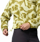 A person wearing the Columbia Womens Helvetia II Cropped Sherpa Half Snap Printed Fleece in a green and cream pattern adjusts the waist drawstring. Only their torso and hands are visible, paired with dark pants.