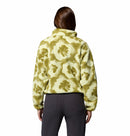 A woman with long brown hair, wearing the Columbia Womens Helvetia II Cropped Sherpa Half Snap Printed Fleece in light yellow and olive green and dark pants, stands facing away from the camera against a plain white background.