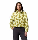 A woman with long brown hair and a neutral expression wears Columbias Womens Helvetia II Cropped Sherpa Half Snap Printed Fleece in yellow-green print, featuring a high collar, snap buttons, PFAS-free material, against a white background with dark pants.
