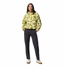 A woman faces forward wearing the Columbia Womens Helvetia II Cropped Sherpa Half Snap Printed Fleece in a yellow and green pattern, paired with dark gray pants and white sneakers, on a white background.