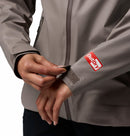 A person adjusts the Velcro cuff strap on the sleeve of a gray Columbia Womens Reign No Shine Waterproof Jacket, with a red and white OutDry logo by the wrist. Only their hands, arms, and torso are visible.