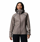 A woman wears a light gray Columbia Womens Reign No Shine Waterproof Jacket with front pockets and black pants, standing against a plain white background, ready for reliable rain protection.