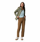 A woman with long brown hair stands facing forward, hands in pockets, wearing a light green Columbia Womens Reign No Shine Waterproof Jacket over a light blue top, brown pants, and white sneakers against a plain white background.