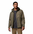 A man wears the Columbia Mens Pouring Adventure™ III Waterproof Hiking Jacket in khaki green over a dark gray t-shirt and tan pants, standing against a plain white background.