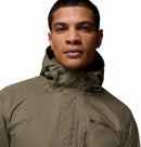 A man wearing a Columbia Mens Pouring Adventure™ III Waterproof Hiking Jacket in olive green, featuring a zippered front and the Columbia logo on the left chest, looks at the camera against a plain white background.