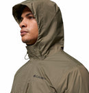 A person faces forward wearing an olive green Columbia Mens Pouring Adventure™ III Waterproof Hiking Jacket with the hood up. Its weatherproof fabric and visible Columbia logo signal reliability for hiking in wet conditions.