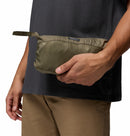 A person in a black shirt and tan pants holds a small, olive green zippered pouch—ideal for packing the Columbia Mens Pouring Adventure™ III Waterproof Hiking Jacket.