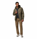 A man wears the Columbia Mens Pouring Adventure™ III Waterproof Hiking Jacket over a dark shirt, tan pants, and gray sneakers, standing against a white background and looking slightly to the right while holding his jacket.