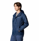 A man wears the Columbia Mens Pouring Adventure™ III Waterproof Hiking Jacket in blue with matching pants, standing with one hand in his pocket and facing left against a white background.