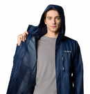 A man with short brown hair wears a blue Columbia Mens Pouring Adventure™ III Waterproof Hiking Jacket with the hood up, holding one side open to show the inner lining. He has a light grey t-shirt underneath. The background is white.