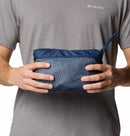 A person wearing a gray Columbia t-shirt and the Columbia Mens Pouring Adventure™ III Waterproof Hiking Jacket holds a blue zippered pouch with a textured front and small carrying strap.