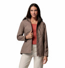 A woman with long dark hair wears the Columbia Womens Pouring Adventure III Waterproof Hiking Jacket over a coral top and beige pants, standing against a plain white background and looking at the camera.