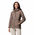 A woman wears a taupe Columbia Womens Pouring Adventure III Waterproof Hiking Jacket with zippered pockets and off-white pants, smiling and looking to the side against a white background.