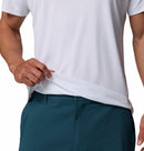 A person wears the Columbia Mens Zero Rules™ Light Technical T-Shirt in white, paired with teal pants. They lift the hem to reveal the moisture-wicking fabric; only their torso and part of their arms are visible.