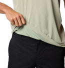 A person in black pants lifts the hem of a Columbia Mens Zero Rules™ Light Technical T-Shirt in light green, revealing a subtle inner pattern.
