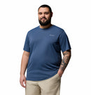 A bearded man with a tattooed forearm stands against a white background, wearing the Columbia Mens Zero Rules™ Light Technical T-Shirt in blue and light khaki shorts, one hand in his pocket and looking relaxed.