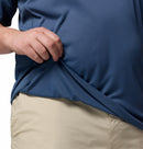 A person in Columbias Mens Zero Rules™ Light Technical T-Shirt lifts the hem, revealing its textured, moisture-wicking inner fabric. Only their hand, part of the arm, and torso are visible as they wear light khaki shorts.
