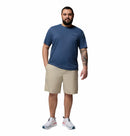 A bearded man stands facing forward in a Columbia Mens Zero Rules™ Light Technical T-Shirt, tan shorts, and white sneakers. He has a tattoo on his left forearm, one hand in his pocket, and is set against a plain white background.