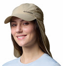 A woman in a light blue shirt smiles at the camera, wearing a Columbia Schooner Bank II Cachalot Hat (light beige, UPF 50, with neck flap) against a white background.