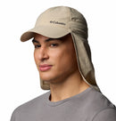 A person wearing a beige Columbia Schooner Bank II Cachalot Hat with a neck flap and a gray crew-neck shirt, posing against a plain white background.
