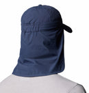 A person wearing a Columbia Schooner Bank II Cachalot Hat in navy blue, featuring UPF 50 protection and an extended neck flap, is viewed from behind against a plain white background.